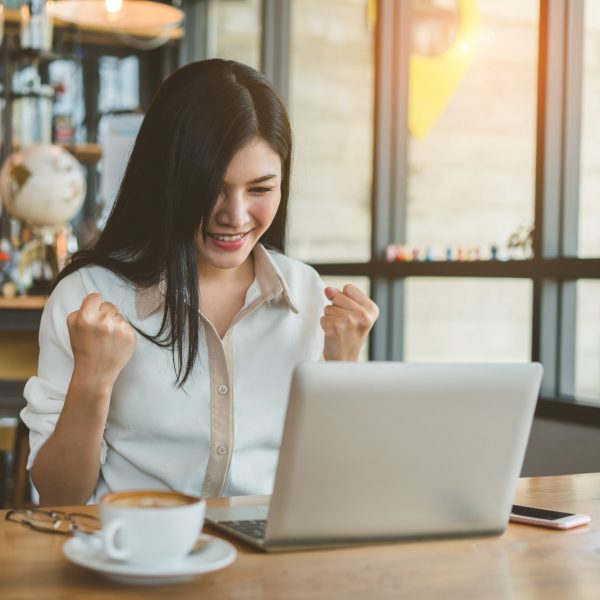 Freelancer beautiful asian woman success business project with digital laptop computer happy and relax at workplace coffee shop in the evening near windows.